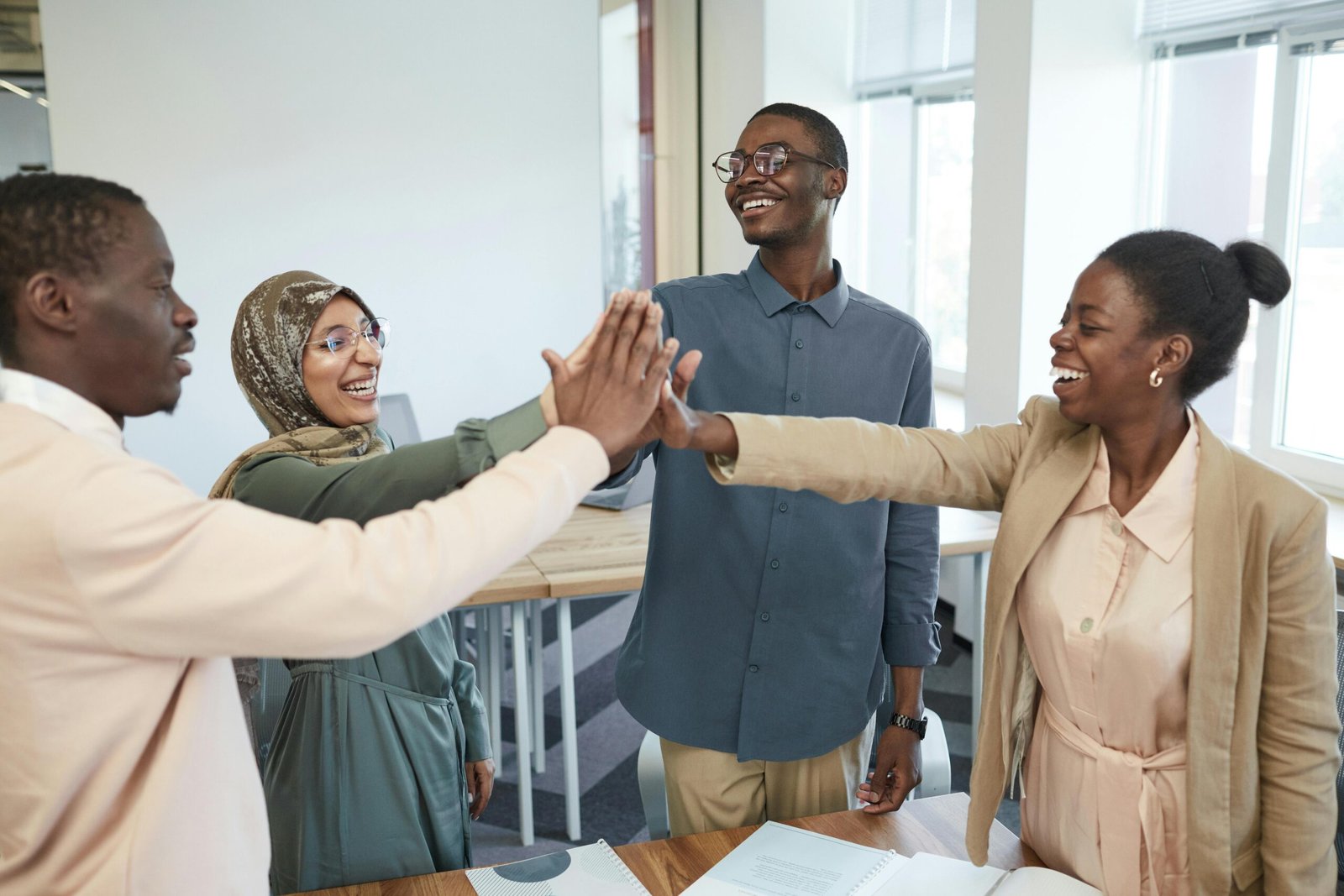Featured A joyful group of diverse colleagues high-fiving each other in an office, symbolizing teamwork and collaboration.