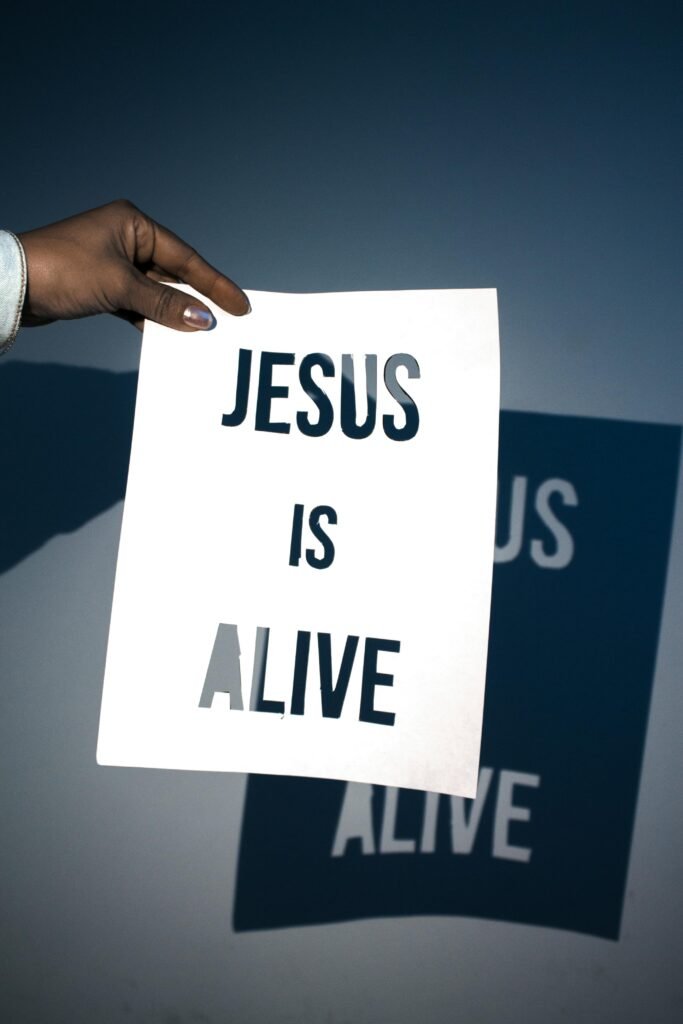 A person holding a white paper with the message 'Jesus is Alive' against a blue background.