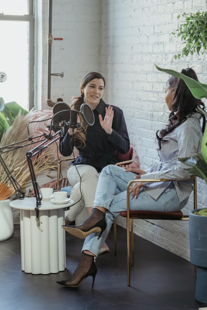 Two women in a modern studio engaging in a podcast conversation with microphones.