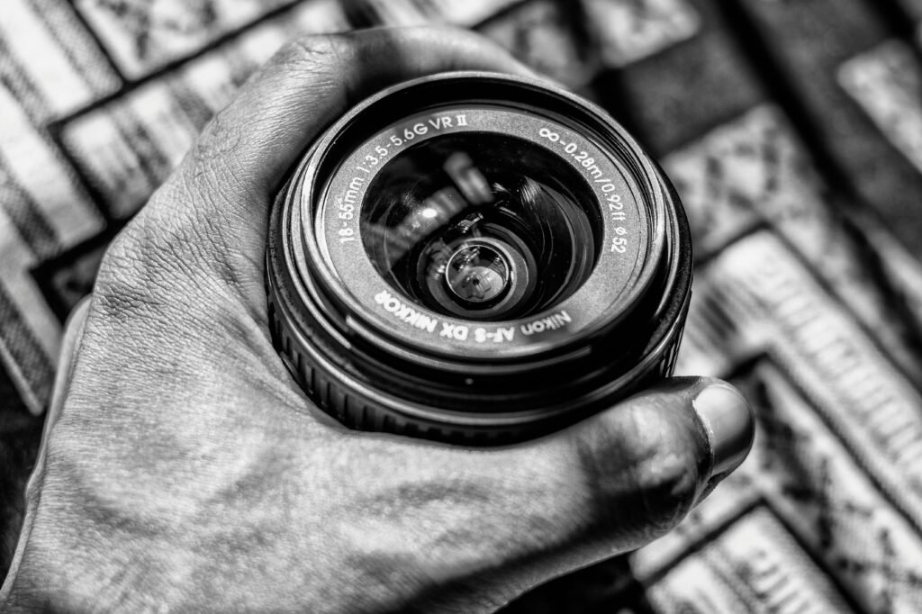 Shaping the African Narrative through a Christian Lens: Our Mission and Vision Black and white image of a Nikon camera lens being held, showcasing classic photography equipment.